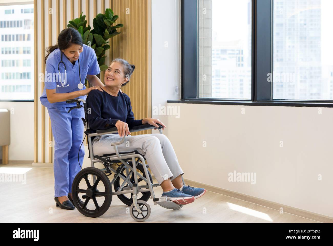 Physiotherapeutin in blauer Uniform-Massage einer älteren Schulter im Rollstuhl zur Schmerzlinderung. Atmosphäre im Gemeindegesundheitszentrum. Stockfoto