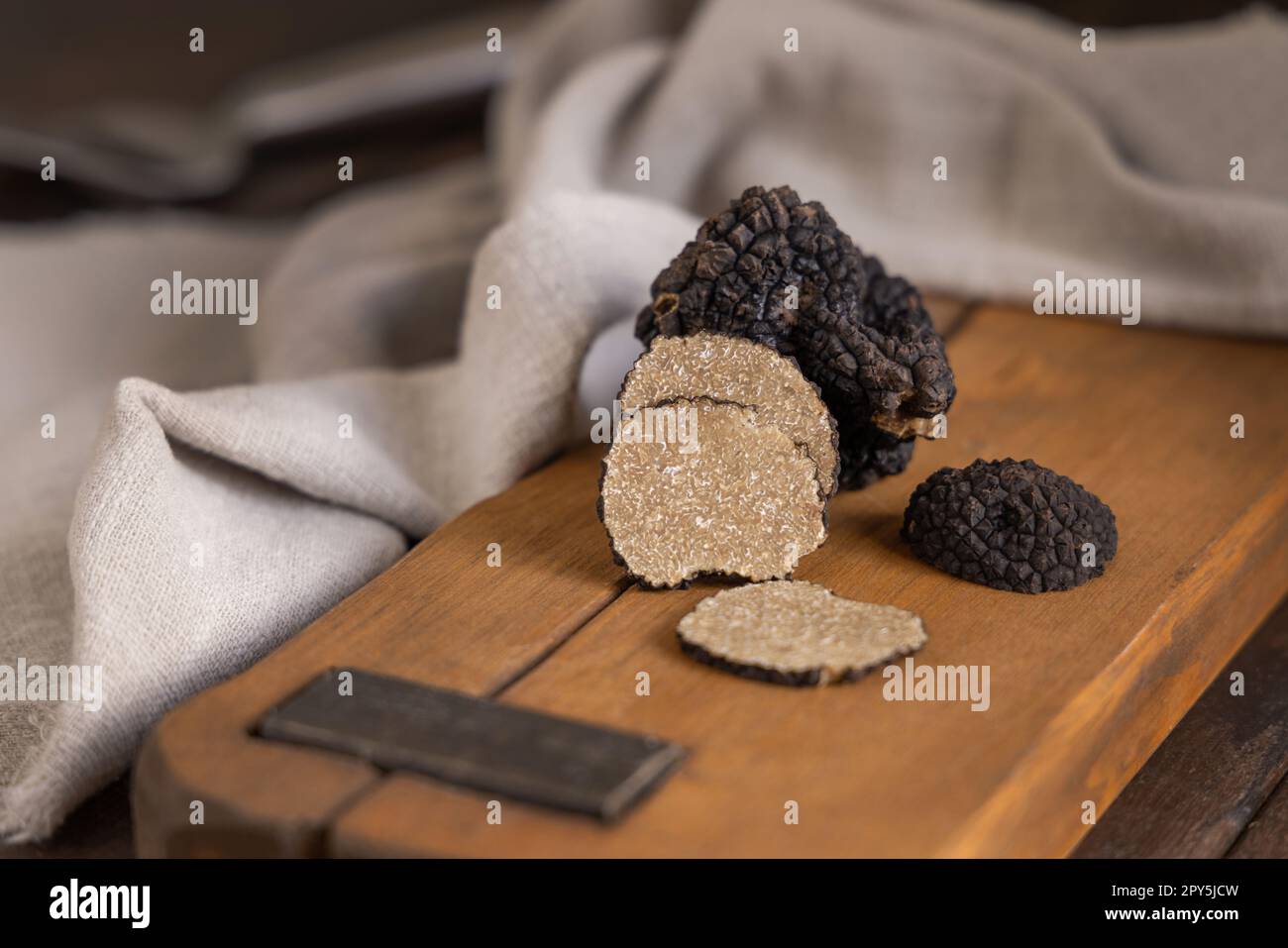 Ganze und geschnittene schwarze Trüffel, Pilze auf Holzbrett auf dunkelbraunem Tisch, Nahaufnahme Stockfoto