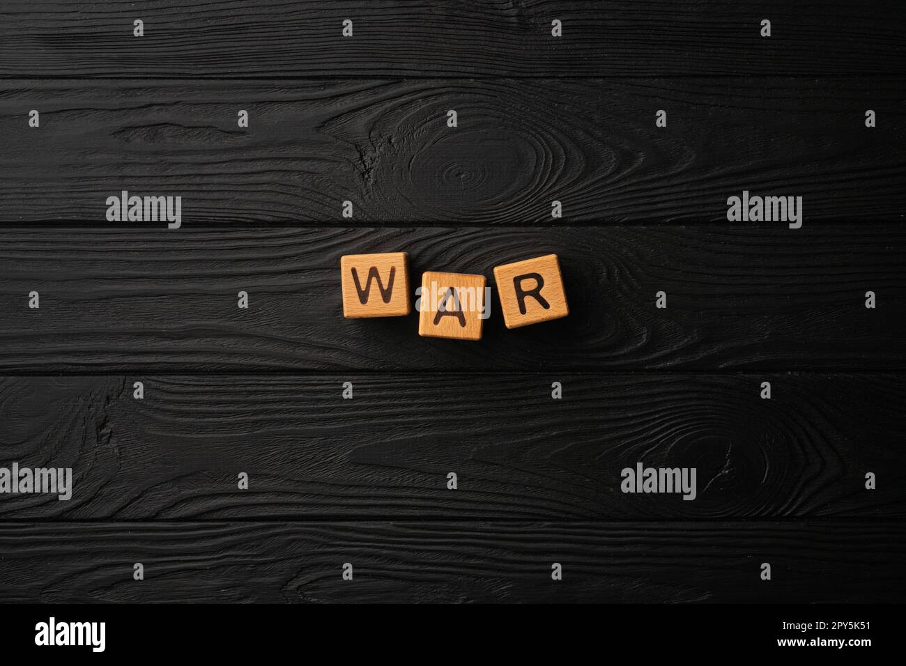Hellgelbe Holzwürfel mit Buchstaben bilden das Wort "Krieg" auf einem schwarzen Holztisch. Flach liegend, Draufsicht. Stockfoto