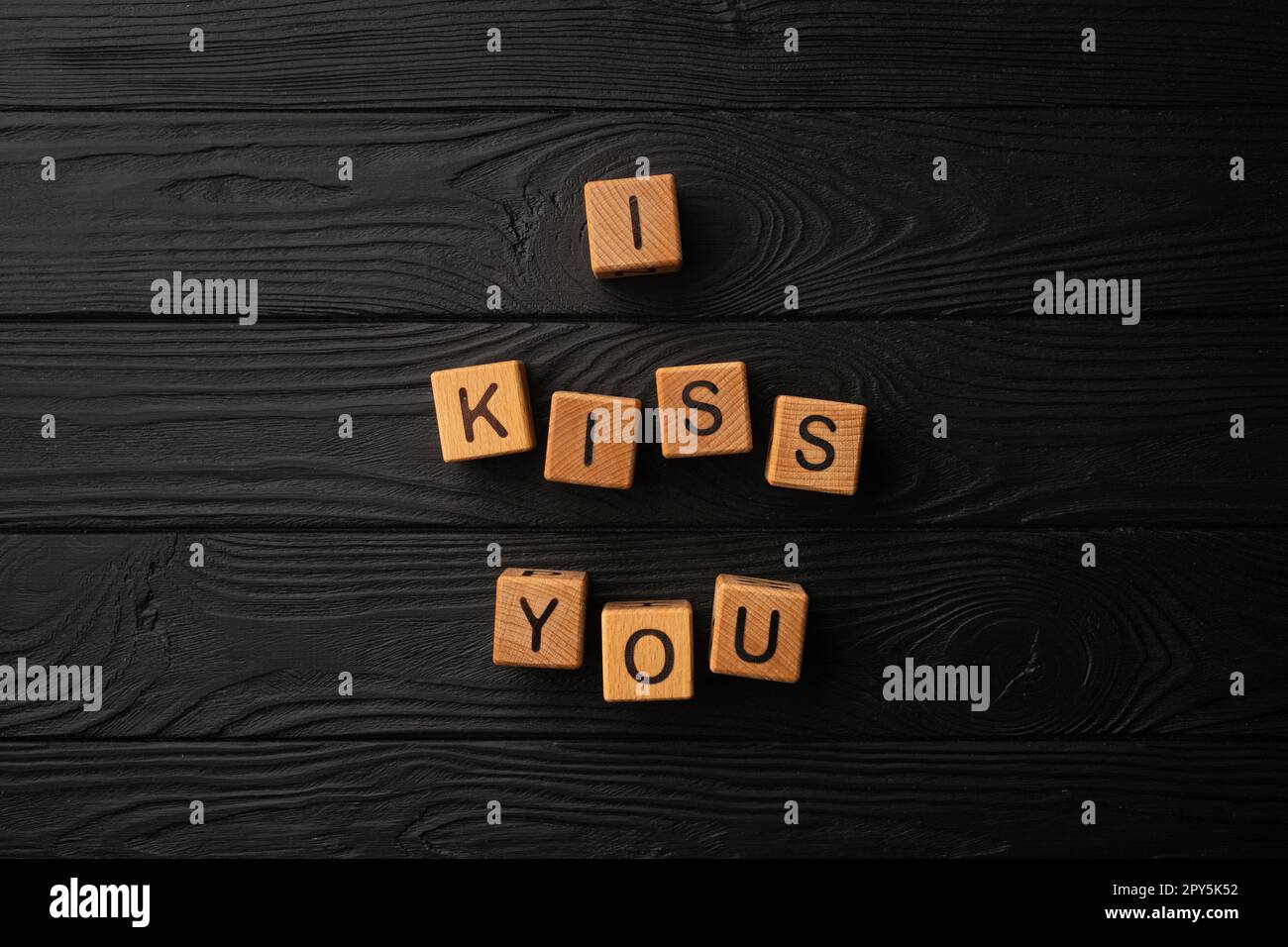 Holzwürfel mit dem Satz "Ich küsse dich" auf schwarzem Hintergrund - ein Holztisch. Worte des Kusses bestehen aus Buchstaben aus Holz für deine Freundin, deinen Freund, deine Frau, deinen Ehemann, für die Valentinstagsgrüßung einer romantischen Postkarte. Stockfoto