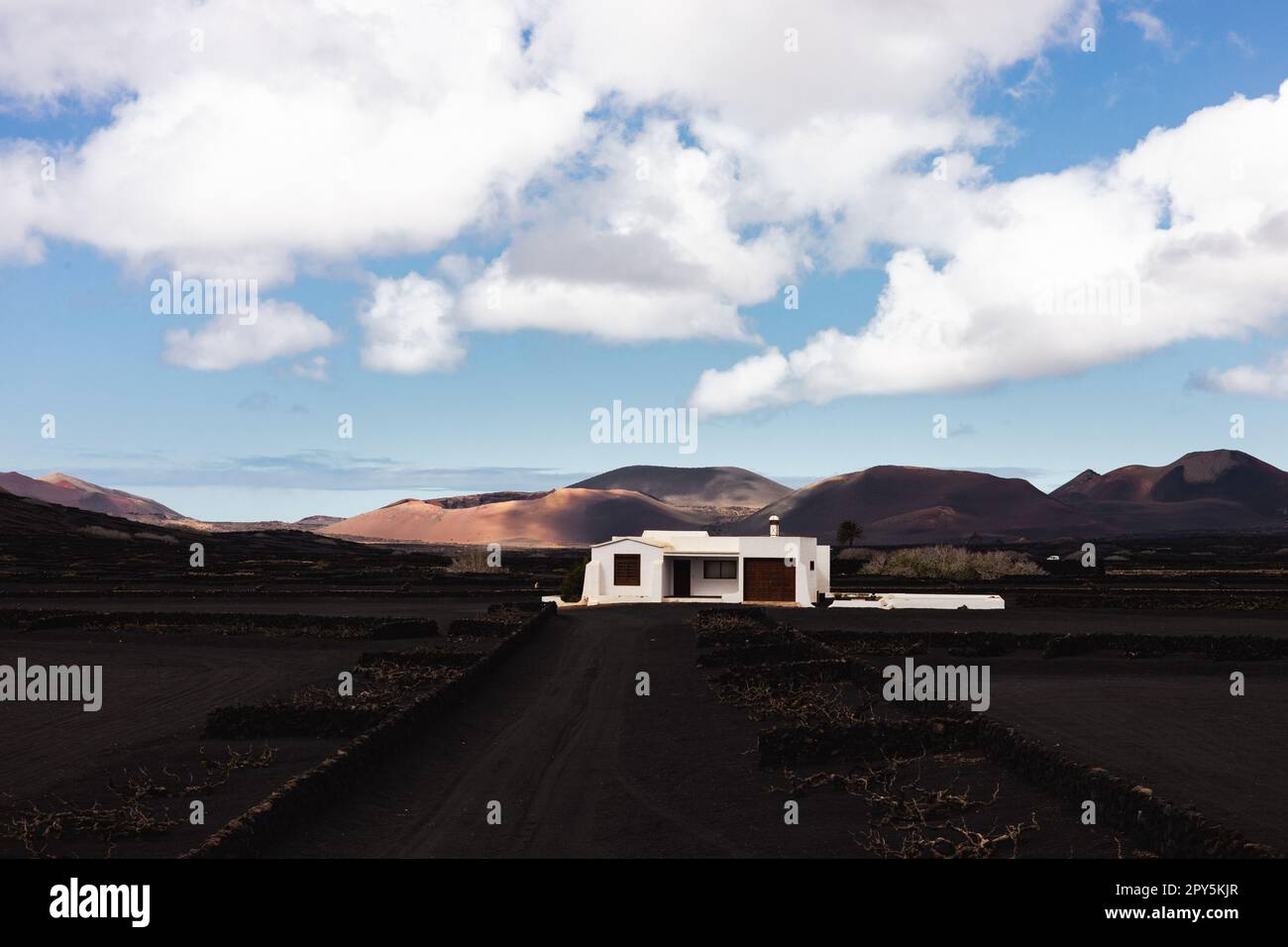 Traditionelles weißes Haus in schwarzer vulkanischer Landschaft der Weinanbauregion La Geria mit Blick auf den Timanfaya-Nationalpark auf Lanzarote. Touristenattraktion auf Lanzarote, Kanarische Inseln, Spanien. Stockfoto