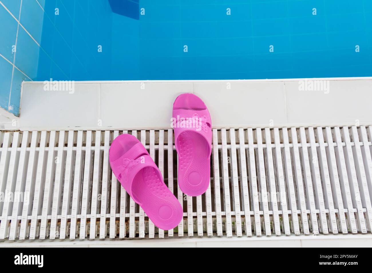 Pinke Hausschuhe stehen am Pool mit blauem Wasser an einem hellen, sonnigen Tag. Stockfoto