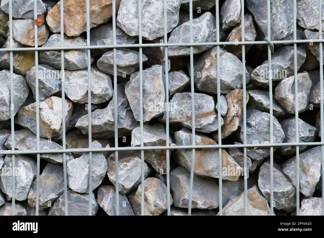 Rohe Felsen und graue Steinwände als Natursteinhintergrund mit zerkleinertem und rauem Material, das in Metallgitter gestapelt ist, als massiver Rand in grauen Farben als natürlicher mineralischer Hintergrund für Gärten Stockfoto