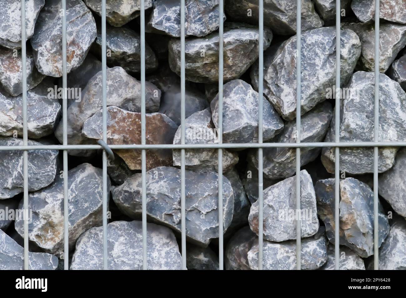 Rohe Felsen und graue Steinwände als Natursteinhintergrund mit zerkleinertem und rauem Material, das in Metallgitter gestapelt ist, als massiver Rand in grauen Farben als natürlicher mineralischer Hintergrund für Gärten Stockfoto