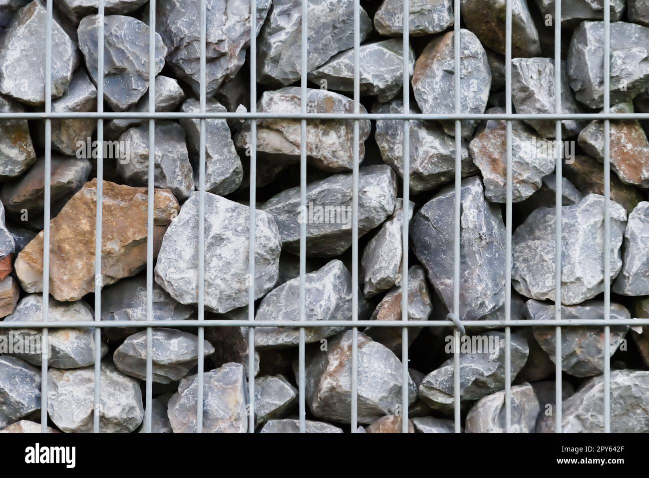 Rohe Felsen und graue Steinwände als Natursteinhintergrund mit zerkleinertem und rauem Material, das in Metallgitter gestapelt ist, als massiver Rand in grauen Farben als natürlicher mineralischer Hintergrund für Gärten Stockfoto