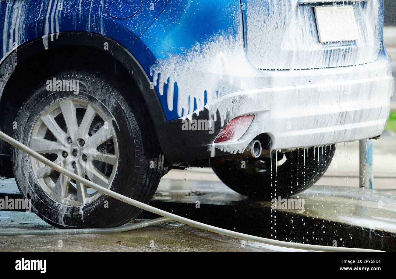 Blaue Autowaschanlage mit weißem Seifenschaum. Autopflegegeschäft. Autoreinigung und -Glanz vor dem Wachsen. Fahrzeugreinigungsdienst mit Antiseptikum und Desinfektionsmittel. Autowaschanlage in der Autopflegewerkstatt. Stockfoto