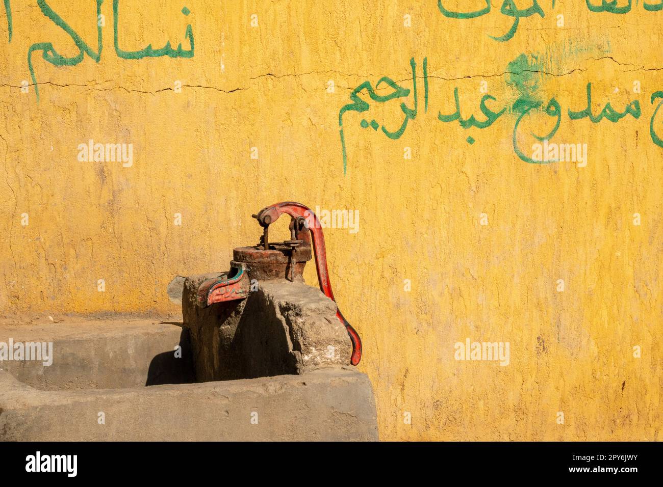 Rote Wasserpumpe gegen eine gelbe Wand mit grünen arabischen Grafitti Stockfoto