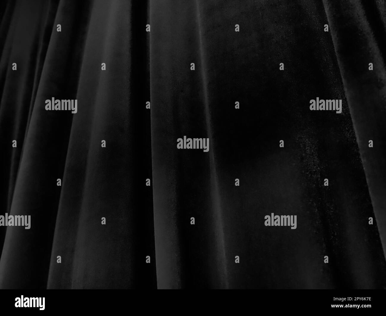Weiche Wellen auf schwarzen Samtvorhängen. Stilisiertes Unschärfe-Bild. Dunkle Vorhänge aus angenehmem Stoff. Falten an den Vorhängen. Abstrakter schwarzer und grauer Hintergrund. Stockfoto