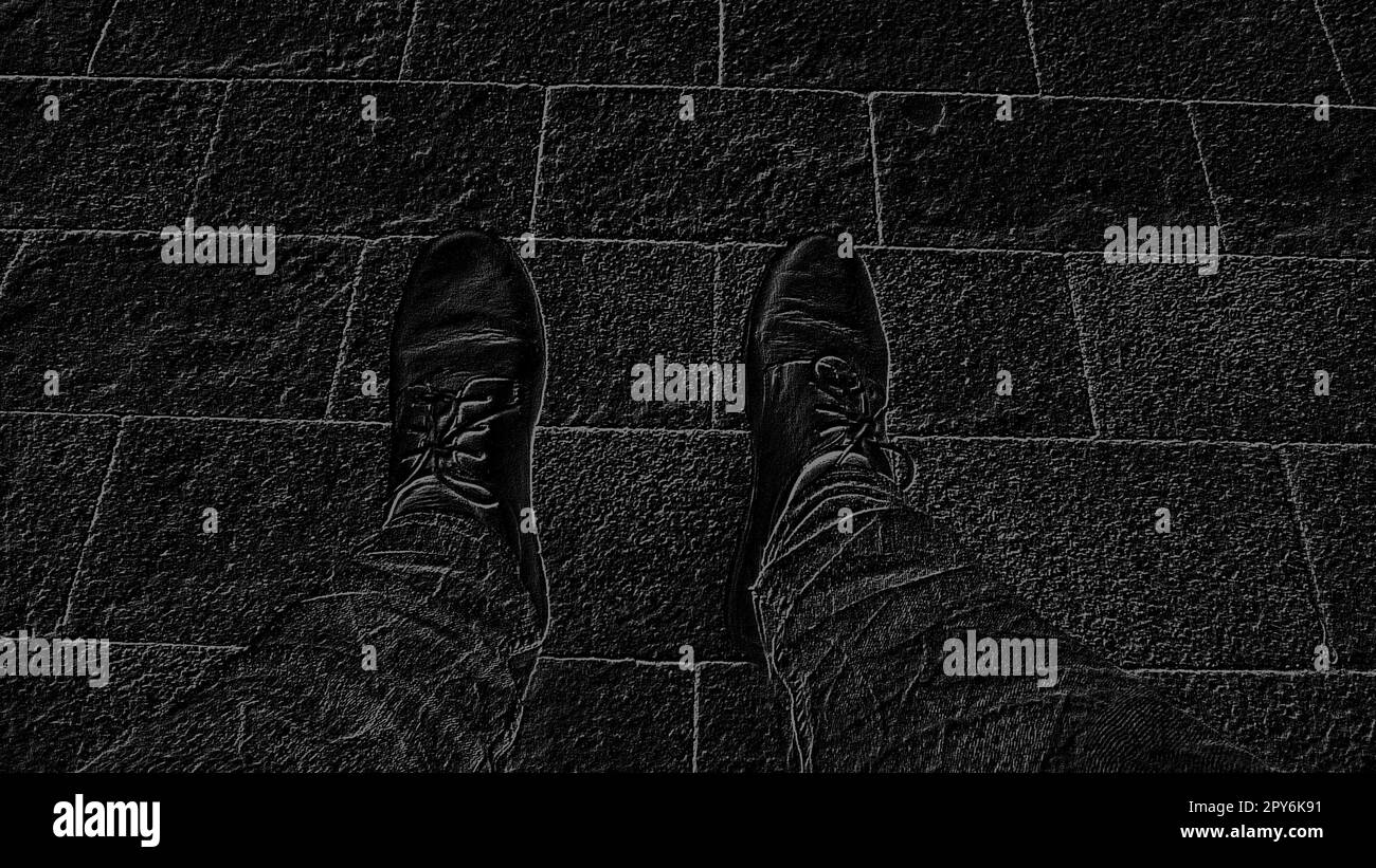 Schwarzweißbild. Füße in Stiefeln vor dem Hintergrund von Straßenfliesen oder der Straße. Zwei Beine eines sitzenden Mannes, von oben fotografiert, während er saß. Stockfoto