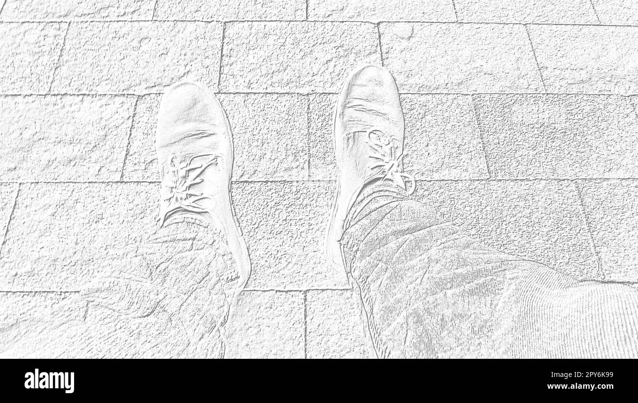 Schwarzweiß- und Graubild. Füße in Stiefeln vor dem Hintergrund von Straßenfliesen oder der Straße. Zwei Beine einer sitzenden Person, von oben fotografiert, während sie sitzt. Horizontales Bild. Stockfoto