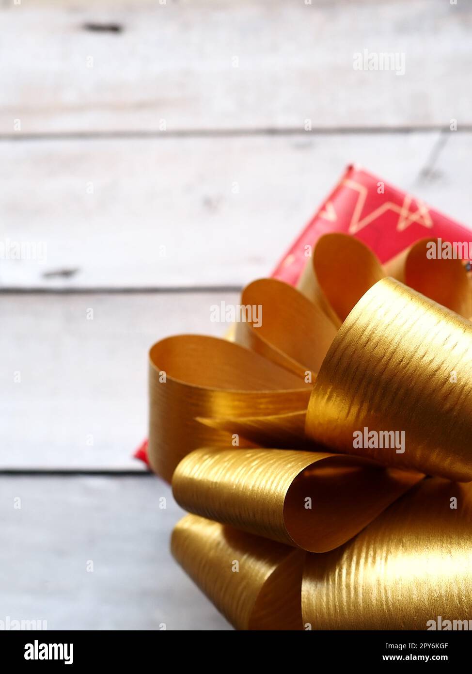 Rote Geschenkbox mit einer großen goldenen Schleife auf einem Holzhintergrund, weiß gestrichen. Geschenk zu Weihnachten, Neujahr, Geburtstag, Muttertag, Hochzeit, Valentinstag. Schöne festliche Dekoration Stockfoto