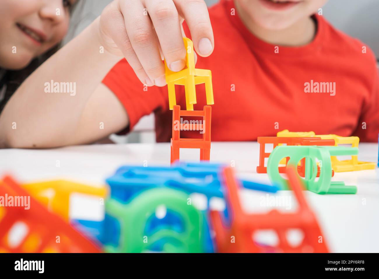 Fröhliche kleine Kinder spielen Spielzeuge, bunte Stühle, die an der Tischschließung sitzen. Junge und Mädchen, gebaut aus kleinen Plastikmöbeln. Stockfoto