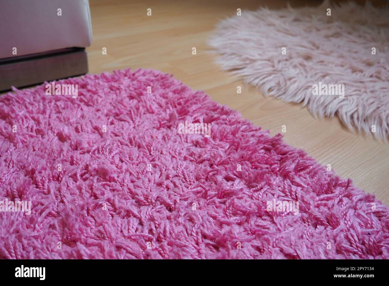Teppich mit langem Flor in Rosa auf einem beigen Laminatboden. Feminine Einrichtung für ein Zimmer oder Schlafzimmer eines Mädchens oder einer Frau. Innendesign in Rosa Farbtönen. Der Fußboden ist Laminat. Die Rolle der Staubmilben bei Allergien. Stockfoto