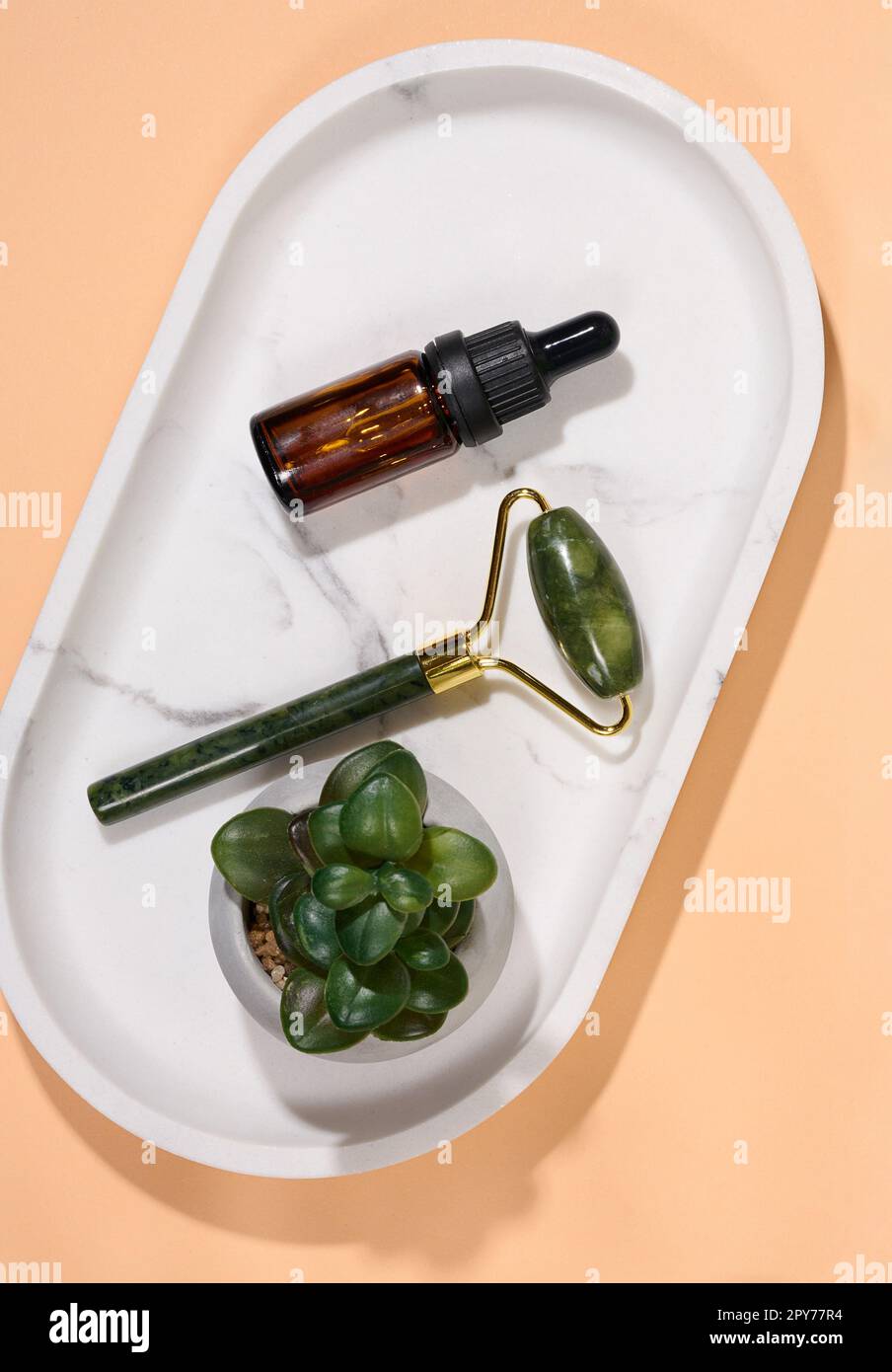 Handmassagegerät für das Gesicht und braune Glasflasche mit Tropfen auf Marmorplatte, Draufsicht Stockfoto