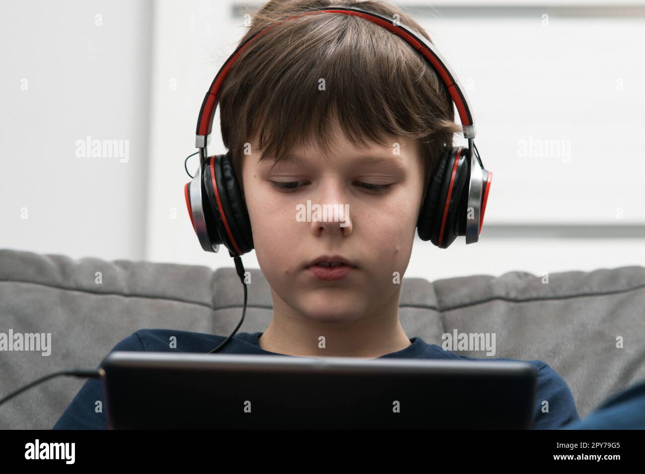 Leidenschaftlicher, konzentrierter brauner Junge mit kabelgebundenen Kopfhörern, der Filme ansieht und Musik mit dem digitalen Pad in den Händen hört Stockfoto