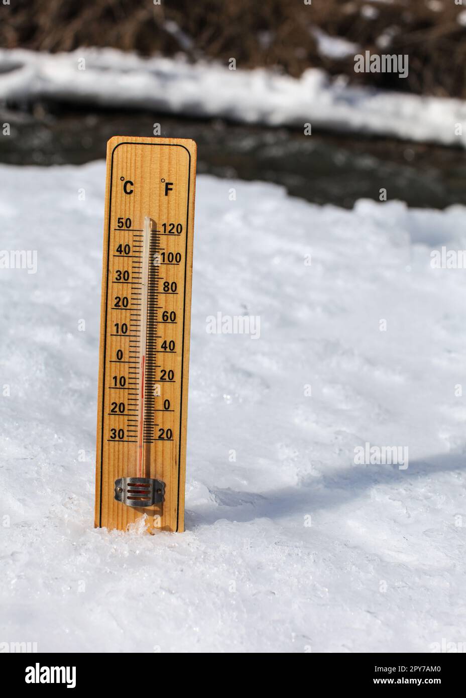 Holzthermometer steht auf Eis auf teilweise gefrorenem Fluss, Sonne scheint, zeigt +3 Grad. Bild zur Veranschaulichung der Winterferien, des langsamen Schneetauens und der kommenden wärmeren Tage Stockfoto