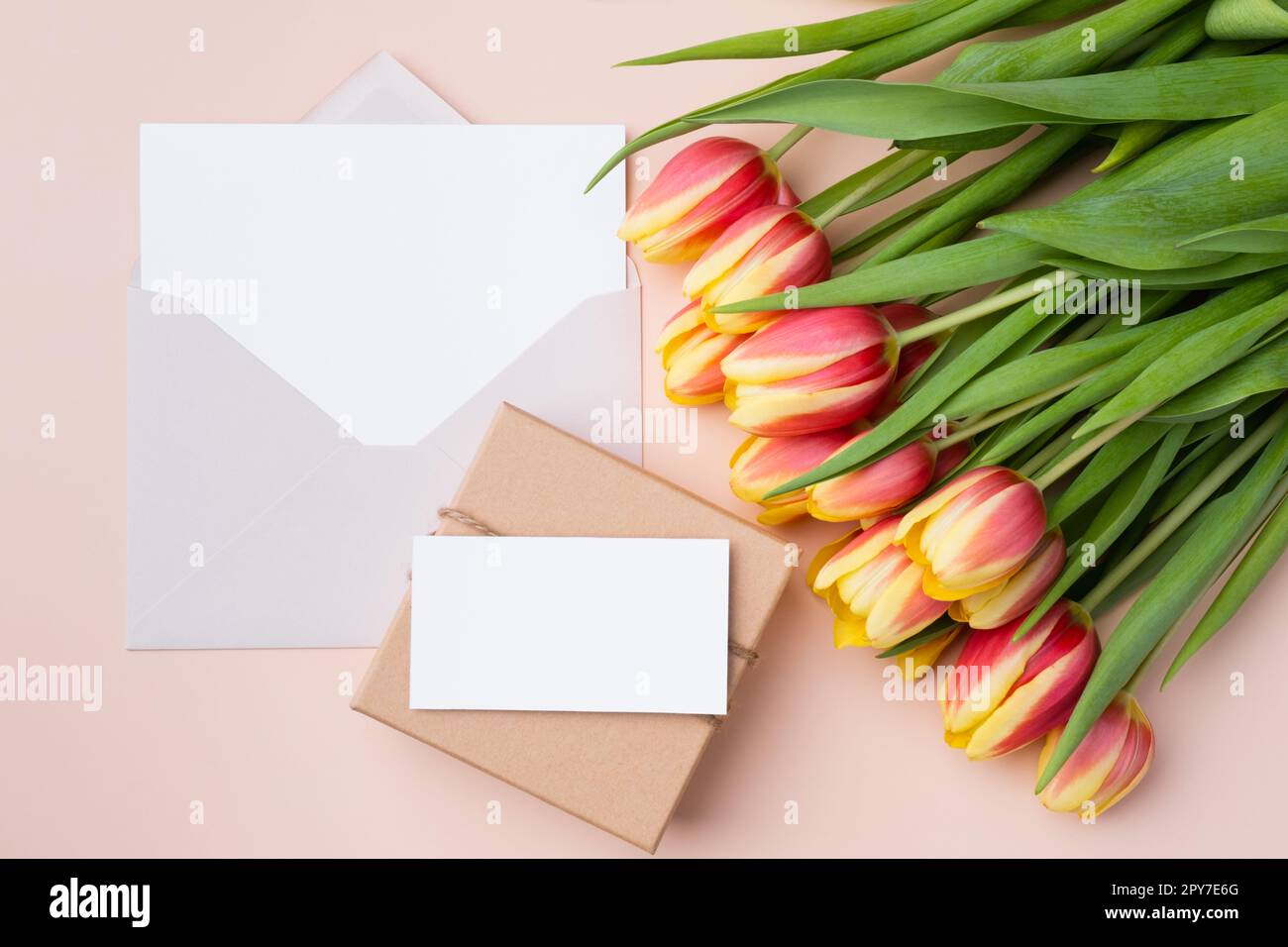 Grußkarten-Mockup oder Dankeskarte-Vorlage. Bouquet von Tulpen und einer Geschenkbox auf beigem Hintergrund. Stockfoto