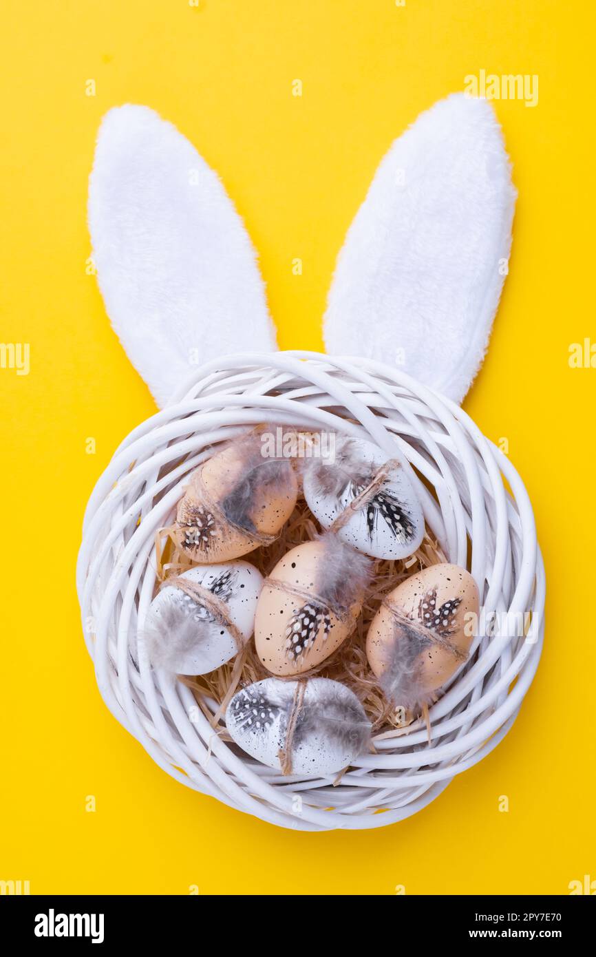 Ostern- oder Frühlingszusammensetzung mit dekorativem weißem Kranz, Wachteleiern und Kaninchenohren auf gelb Stockfoto