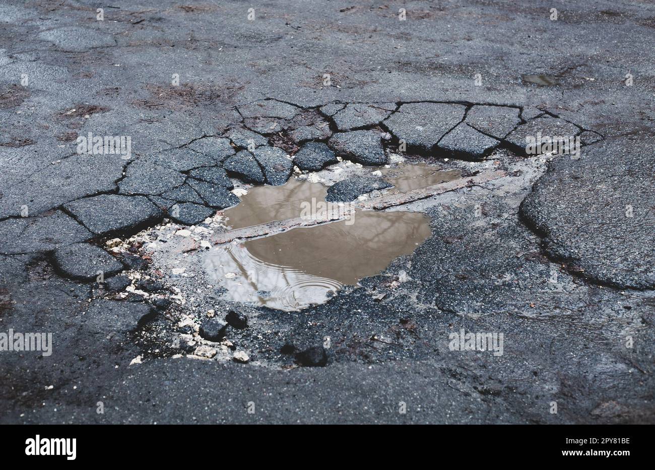 Die befestigte Straßenoberfläche ist beschädigt. Gebrochener Asphalt. Pfütze auf gerissener Straße. Stockfoto