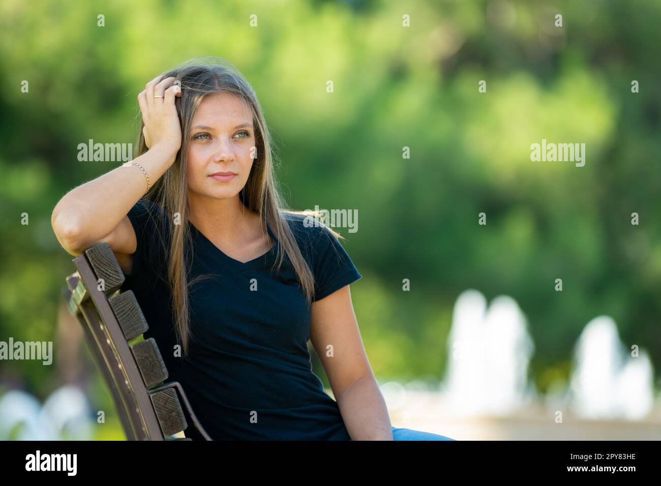 Ein Mädchen sitzt auf einer Bank, die ihren Kopf mit der Hand in Nahaufnahme nach oben streckt Stockfoto