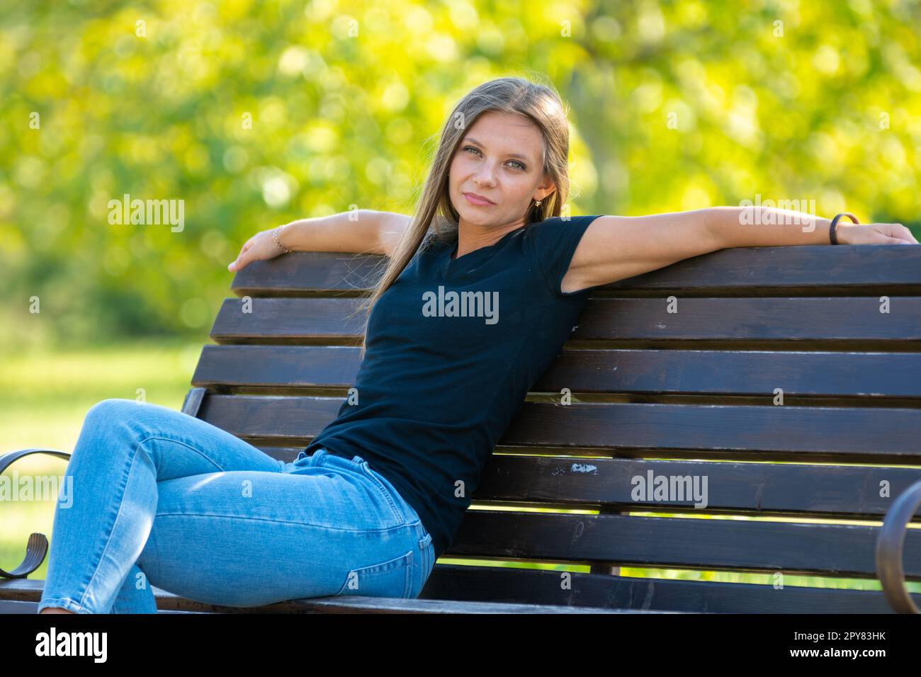Ein Mädchen sitzt auf einer Bank in einem sonnigen Park und schaut in den Rahmen Stockfoto