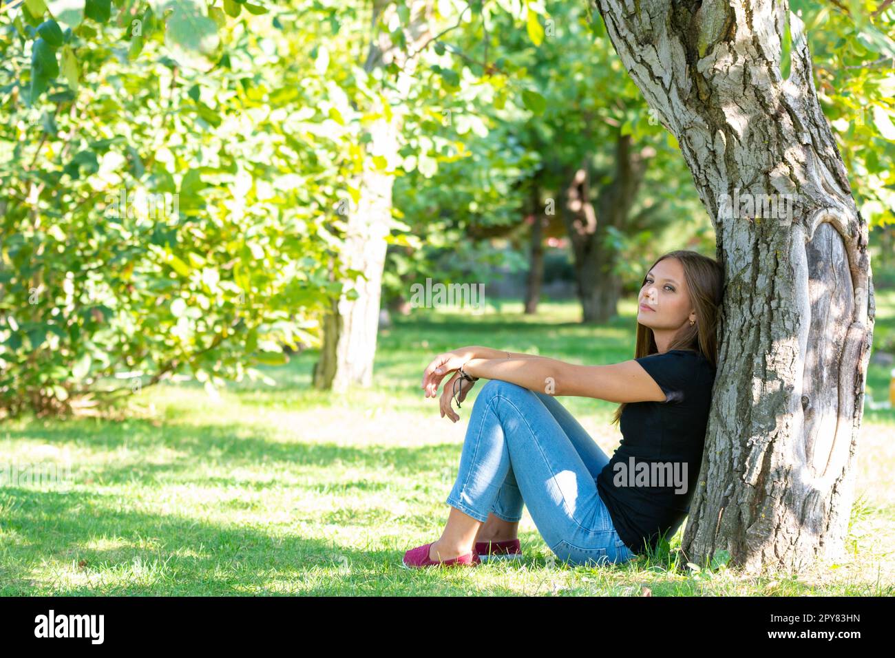 Mädchen sitzt unter einem Baum in einem sonnigen Park Stockfoto