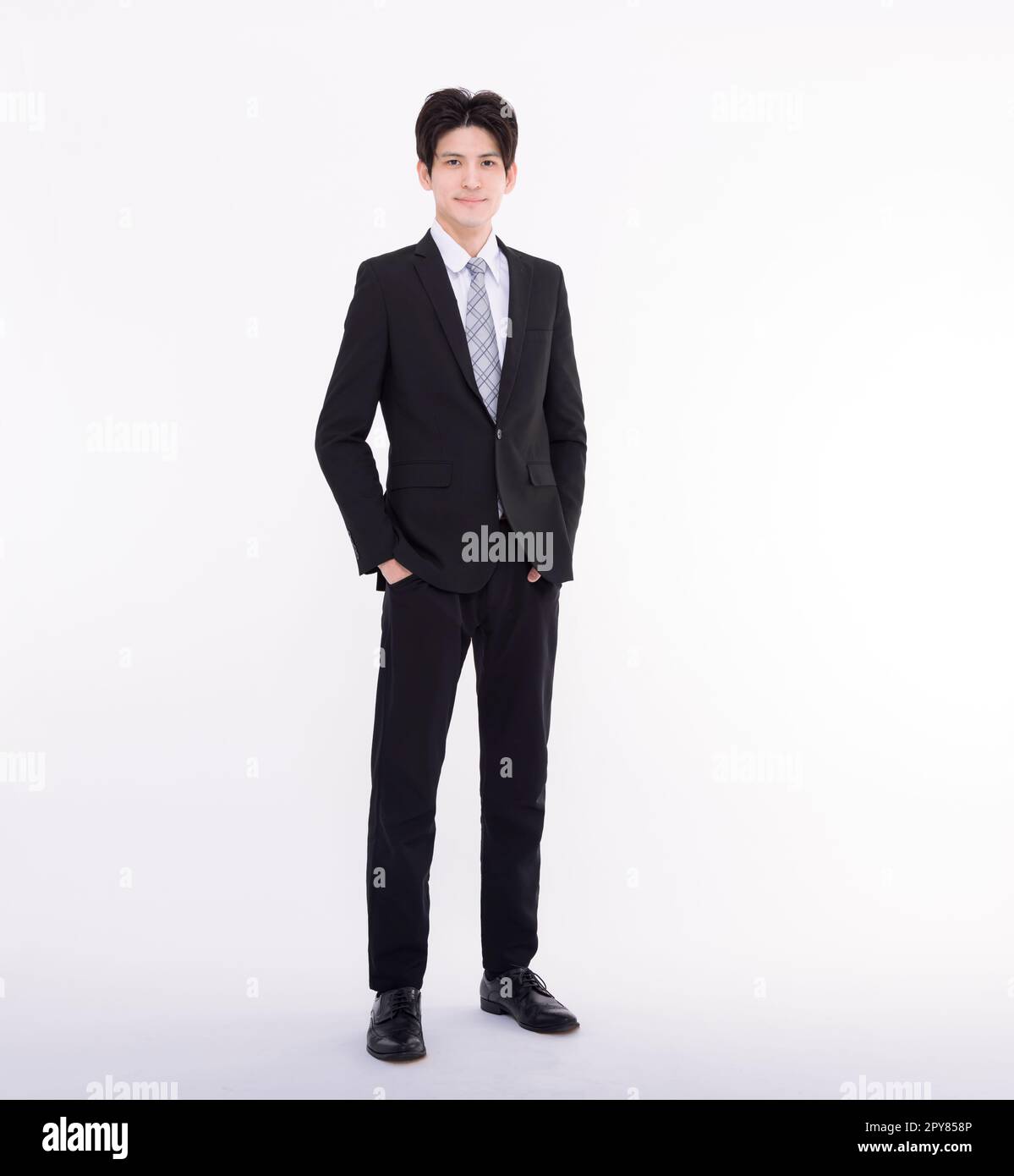 Ein langes Porträt eines jungen Geschäftsmannes, der mit den Händen in den Taschen steht. Stockfoto