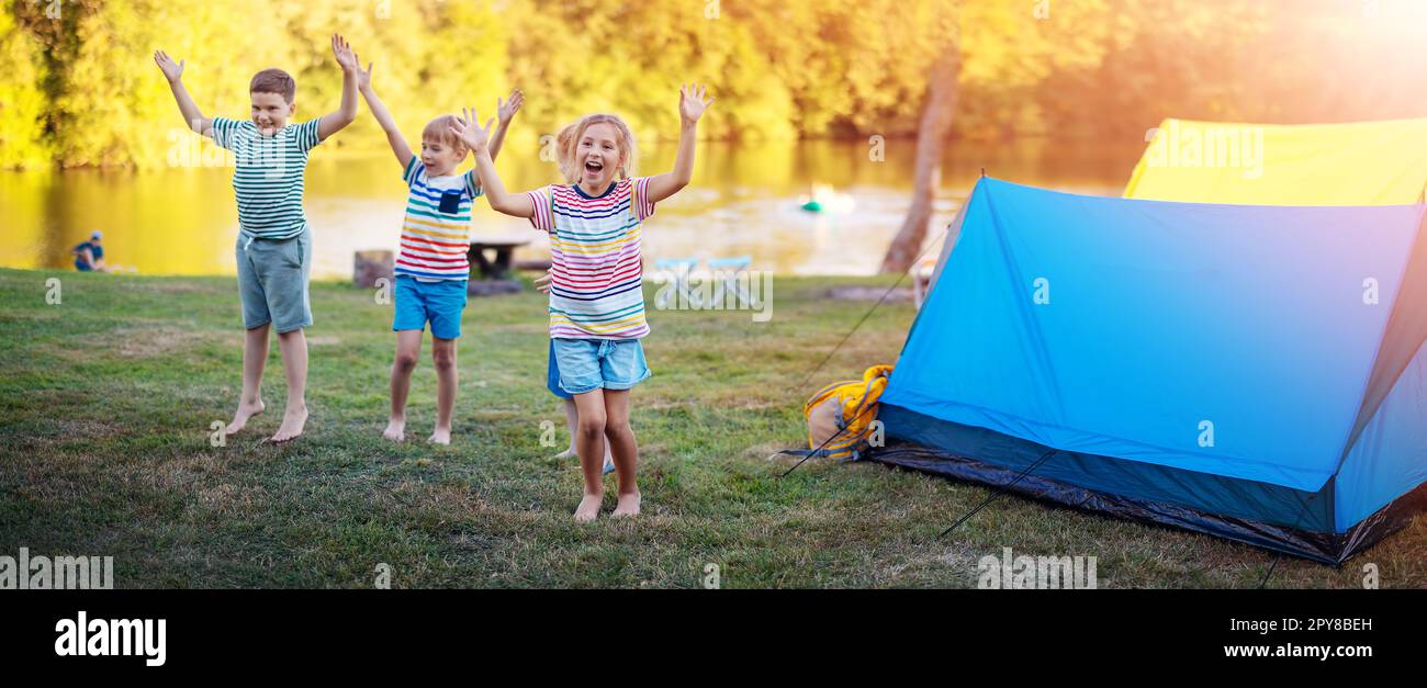 Gruppe von vier Kindern, die in der Nähe farbenfroher Zelte in der Natur spielen. Stockfoto