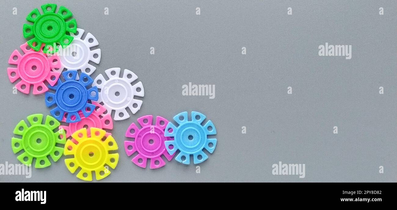 Mehrfarbige Details in Form von Schneeflocken vom Kinderdesigner auf grauem Hintergrund. Rot, gelb, grün, blau, weiß, Rosafarbene Kunststoffscheiben zur Entwicklung der Feinmotorik der Finger Stockfoto