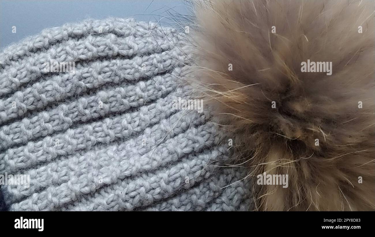 Strickmütze mit Kürbisnaht auf grauem Hauptgrund. Werbung für Winterbekleidung. Wintersaison. Graue und braune Farben. Große Schleifen. Der braune Kürbis aus natürlichem Fell. Stockfoto