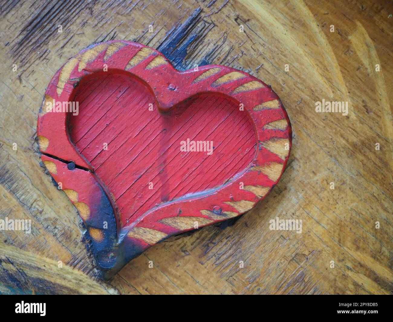 Zimmereiherz auf einer hölzernen Oberfläche und rot gestrichen. Ein Symbol für Liebe und Treue. Postkarte für Glückwünsche oder Anerkennung am Valentinstag. Anzeichen für den Einfluss von Entzündung oder Feuchtigkeit. Stockfoto