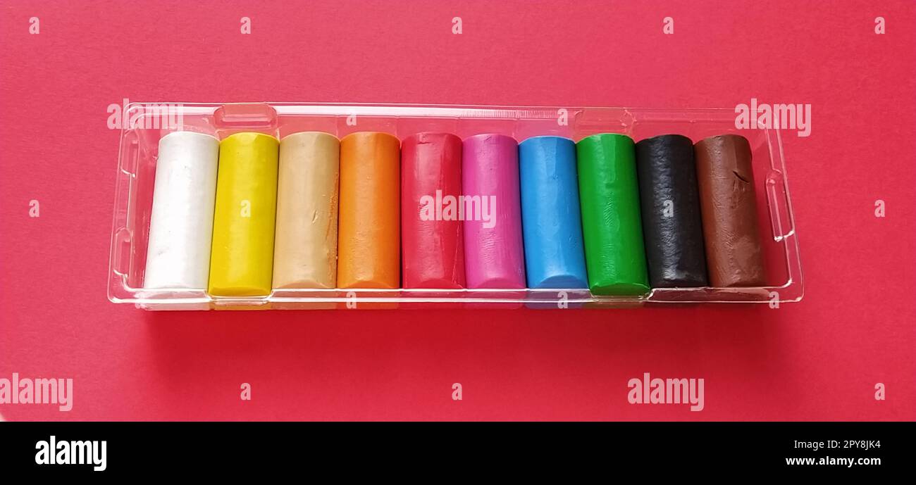 Mehrfarbiges neues Plasticin in Kunststoffverpackung auf rotem Hintergrund. Plastikplatten aus Rot, Pink, Grün, Weiß, Gelb, Braun, blau, schwarz. Set für die Kreativität von Kindern Stockfoto