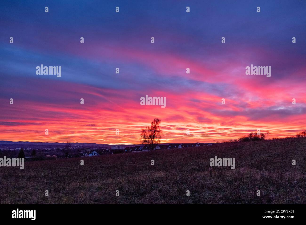 Wunderschöner rosa und roter Sonnenuntergang über den Feldern und einer Kleinstadt Stockfoto