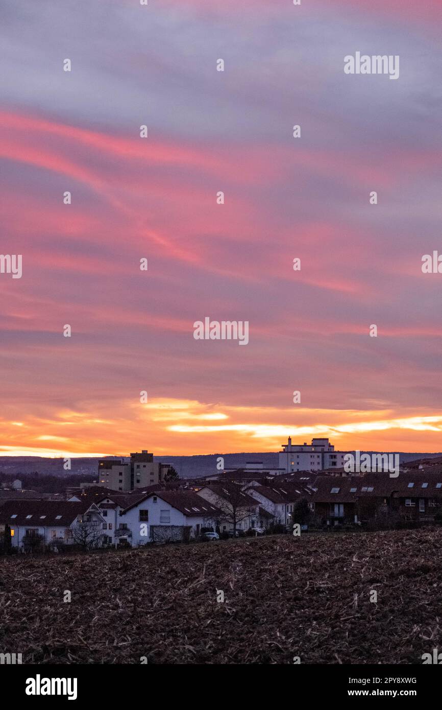 Wunderschöner rosa und roter Sonnenuntergang über den Feldern und einer Kleinstadt Stockfoto