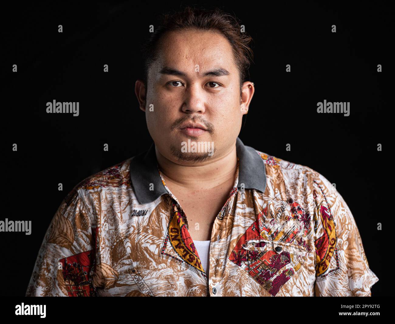 Porträt eines asiatischen Mannes, das vor einem horizontalen Bild mit schwarzem Hintergrund in die Kamera schaut Stockfoto