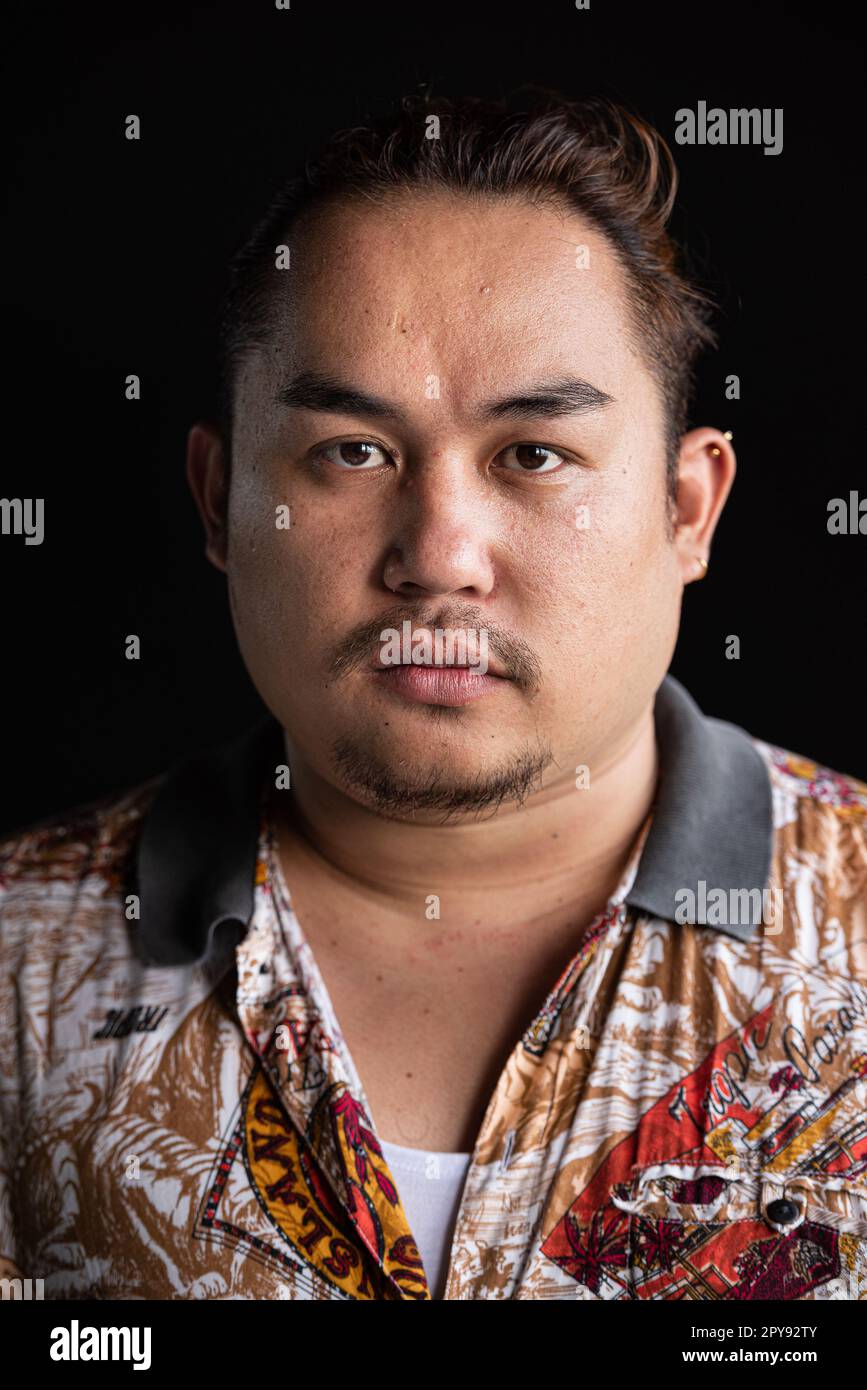 Porträt eines asiatischen Mannes, das vor einem vertikalen Bild mit schwarzem Hintergrund in die Kamera schaut Stockfoto