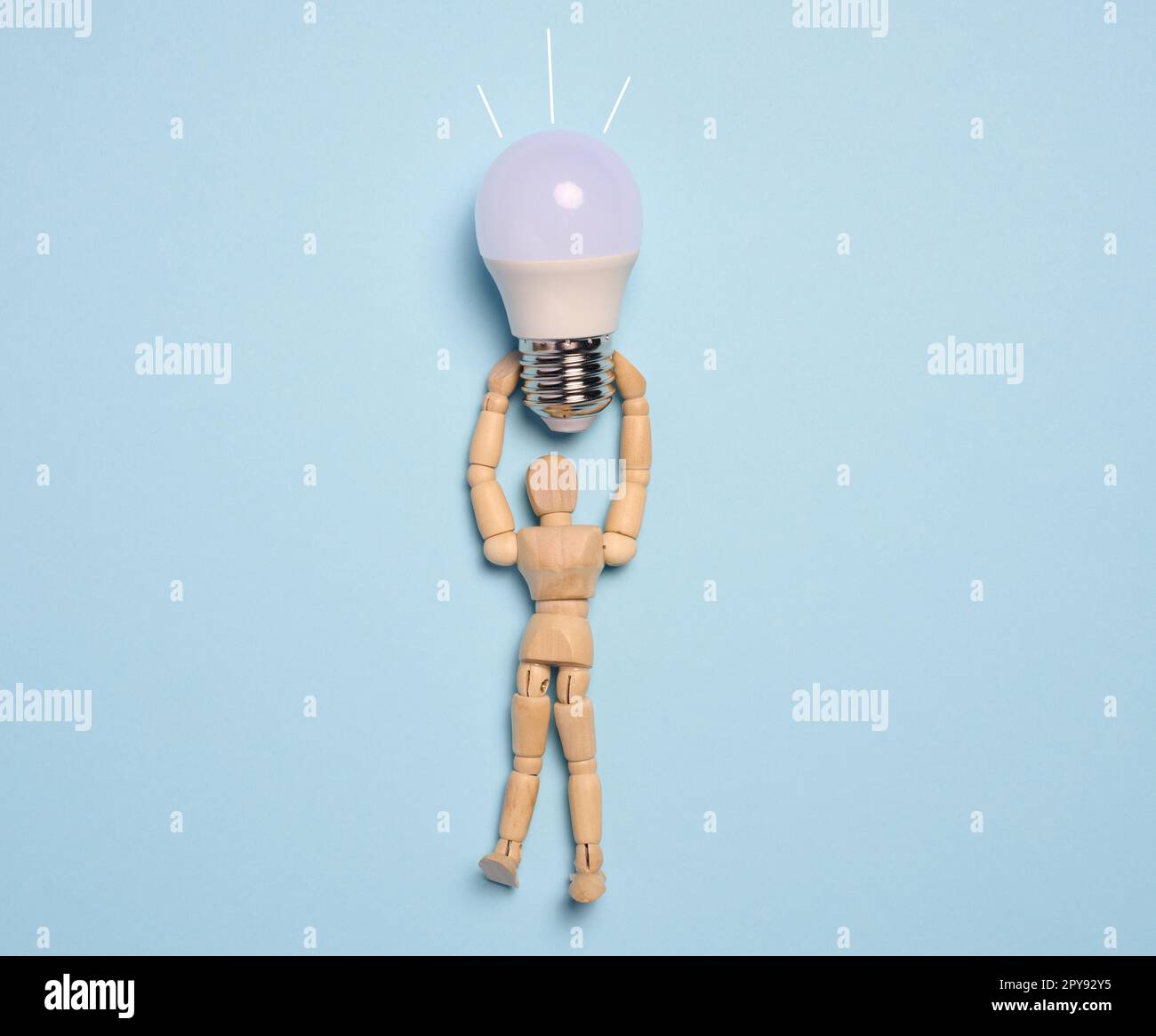 Eine Schaufensterpuppe aus Holz hält eine Glaslampe vor blauem Hintergrund und repräsentiert das Konzept der Suche nach neuen Ideen und optimalen Lösungen Stockfoto