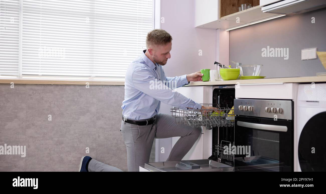 Junger Mann, Der Trinkglas Aus Der Spülmaschine Nimmt Stockfoto