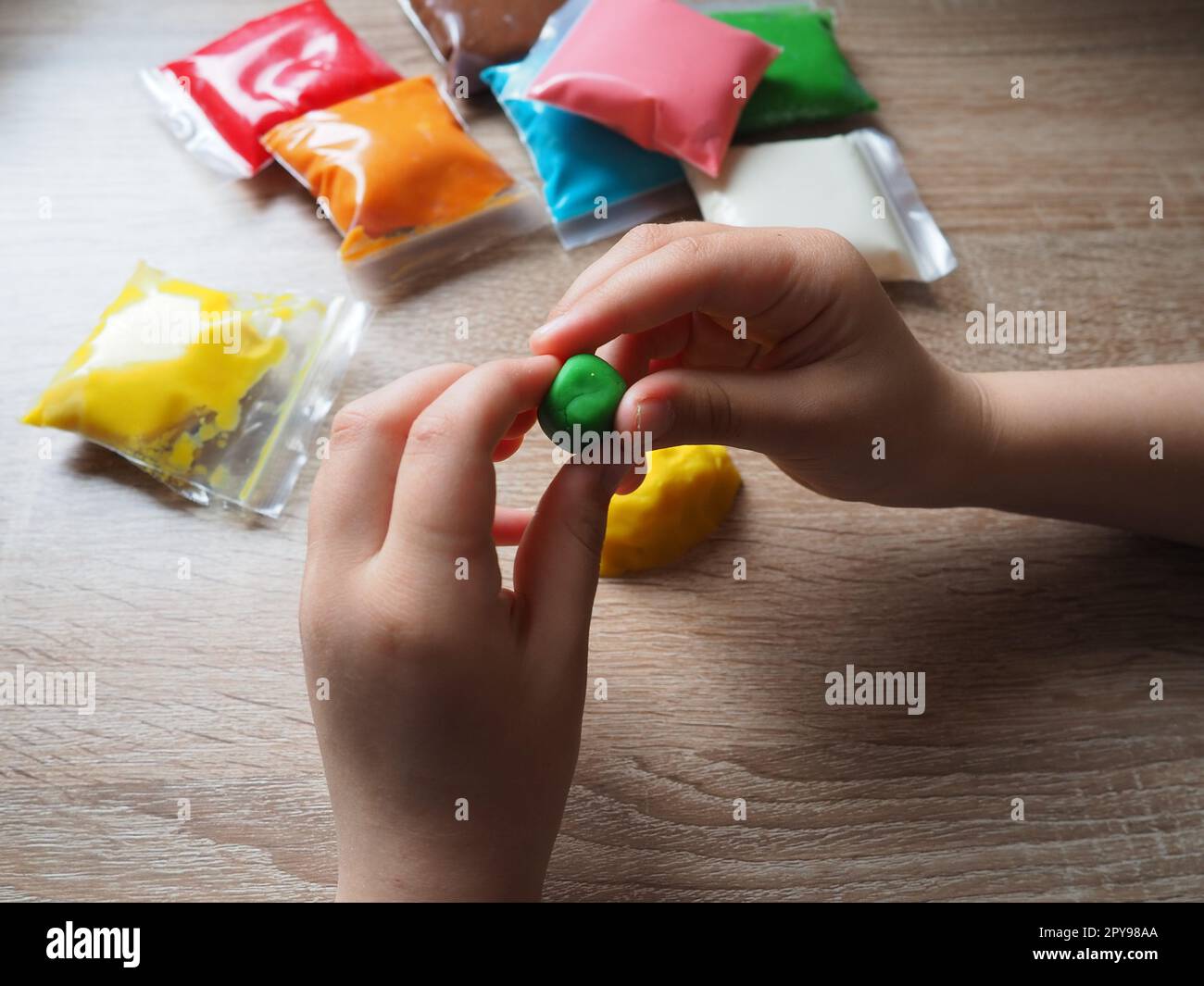 Kinderhände zerknittern weiches Plastikin. Packungen mit Plastin liegen auf dem Tisch. Kreativität zur Entwicklung der Feinmotorik der Hände. Erstellen einer Gussform oder eines Modells aus Plasticine Stockfoto