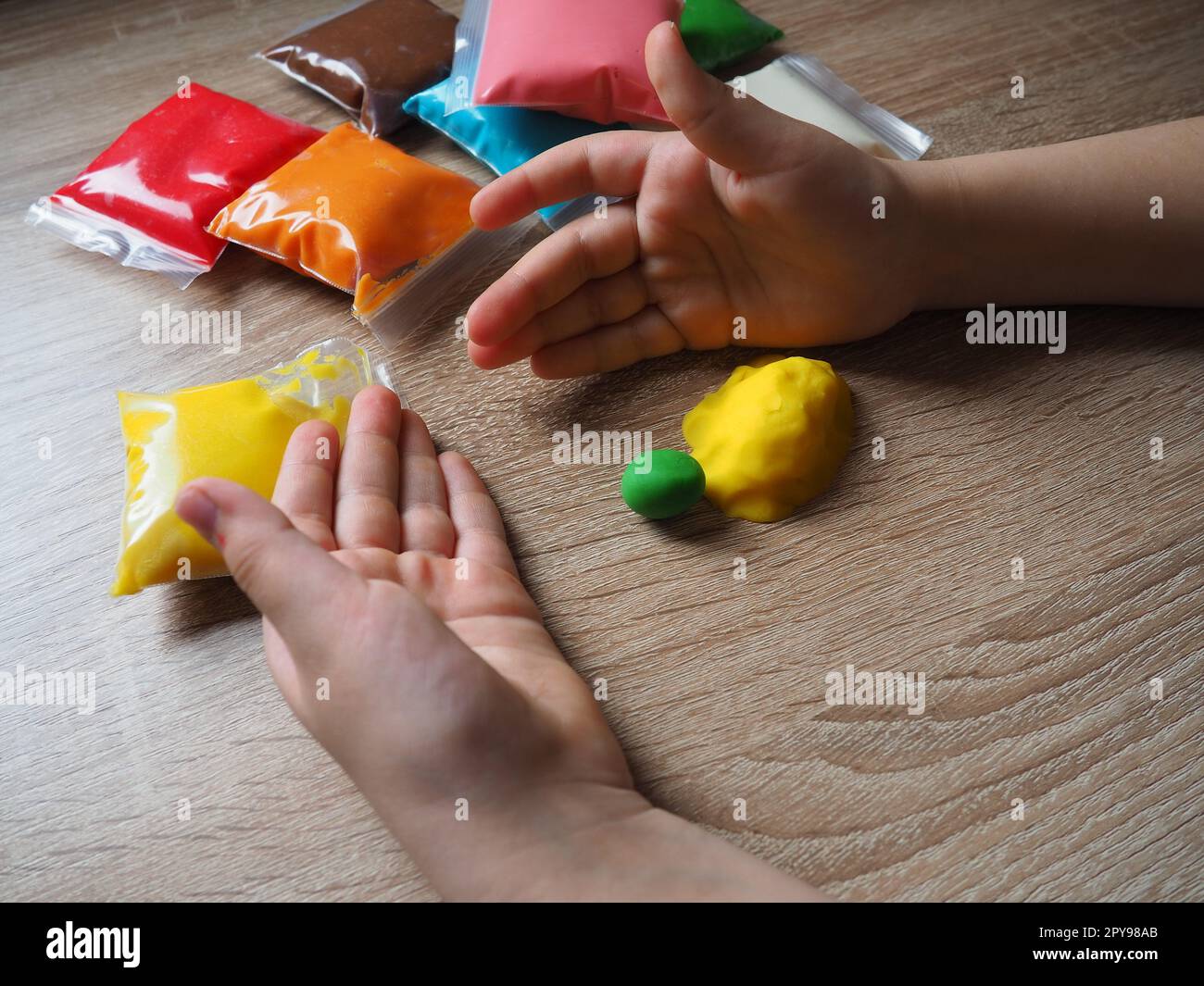 Kinderhände zerknittern weiches Plastikin. Packungen mit Plastin liegen auf dem Tisch. Kreativität zur Entwicklung der Feinmotorik der Hände. Erstellen einer Gussform oder eines Modells aus Plasticine Stockfoto