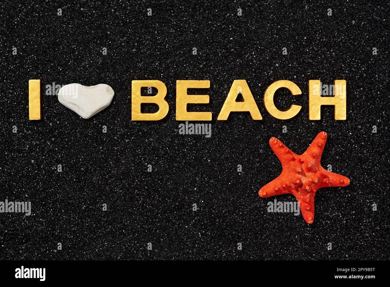 I Love Beach - Goldene Buchstaben in schwarzem Sand und Seesternen Stockfoto