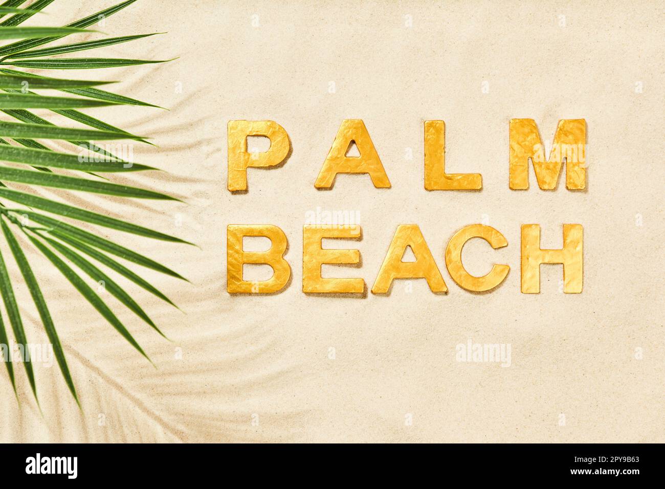 Palm Beach: Goldene Buchstaben im Sand und Palmenblätter Stockfoto