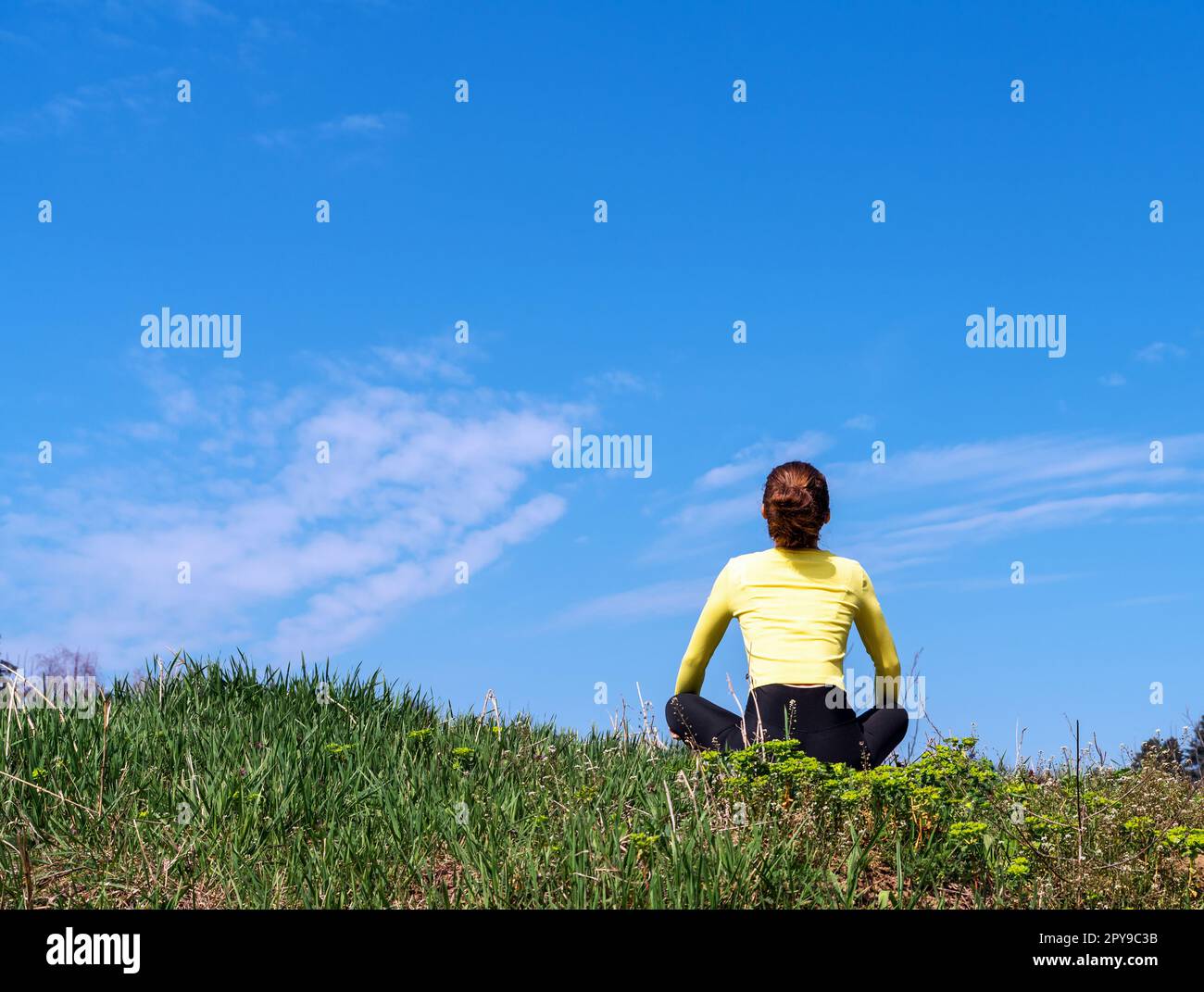 Eine Frau, die auf grünem Gras sitzt und den blauen Himmel sieht, das geistige Wohlbefinden in der Natur. Stockfoto