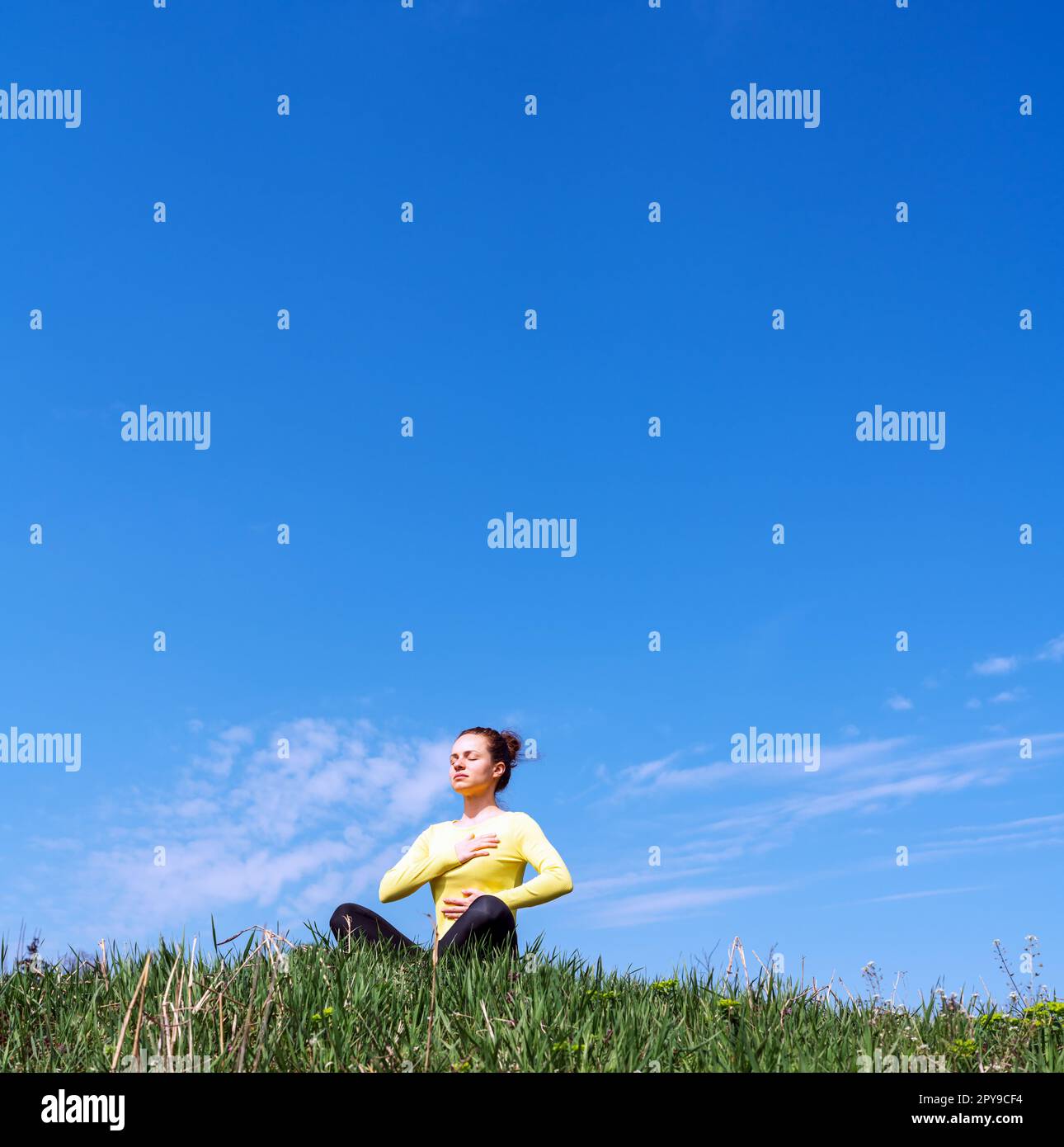Yoga-Atmungsübungen draußen in der Natur, Frau meditiert auf grünem Gras vor blauem Himmel. Stockfoto