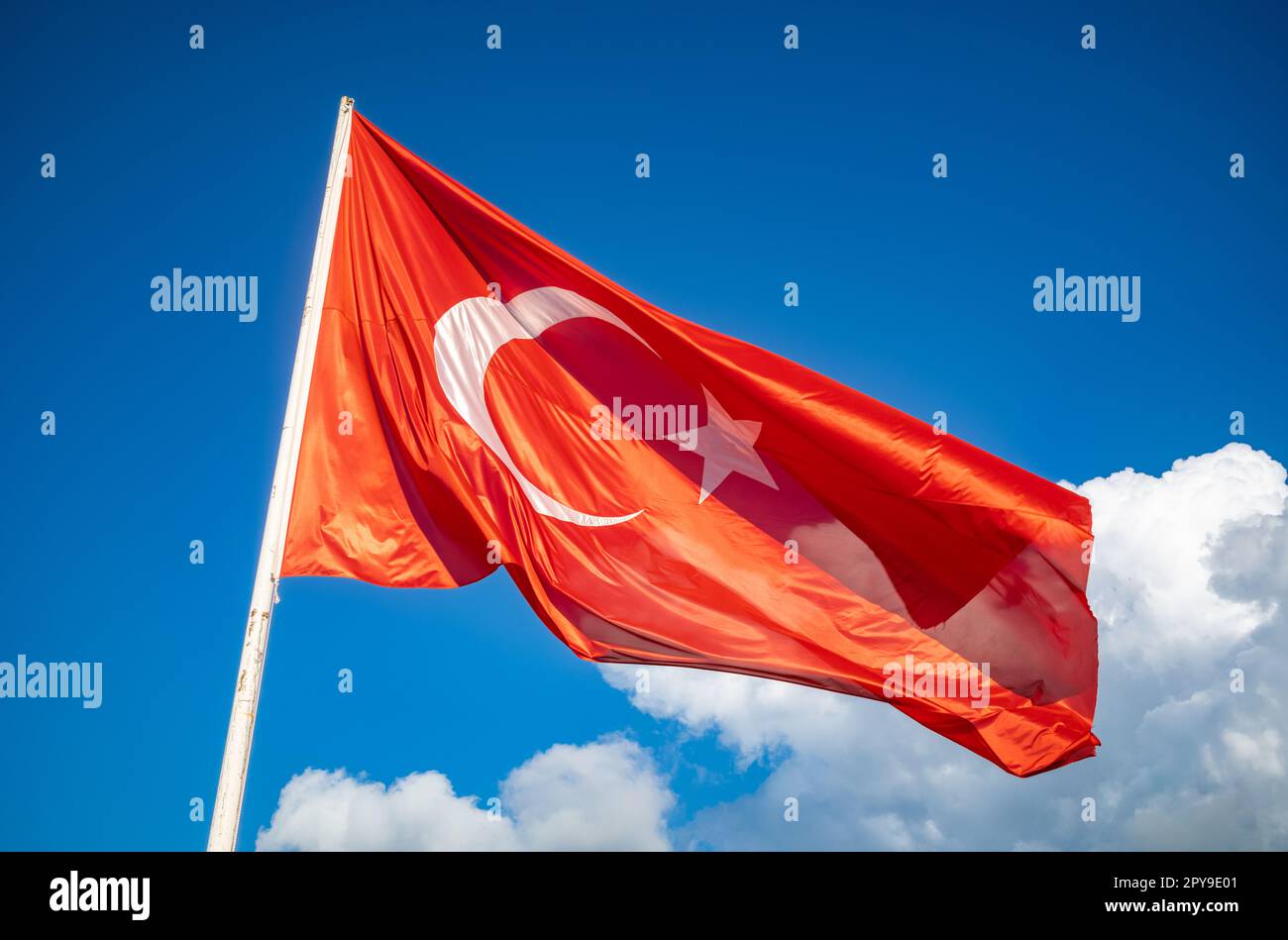 Die majestätische türkische Flagge, hoch und stolz auf einem weißen Fahnenmast, vor dem riesigen blauen Himmel mit weißen Wolken in den Ausläufern der Stockfoto