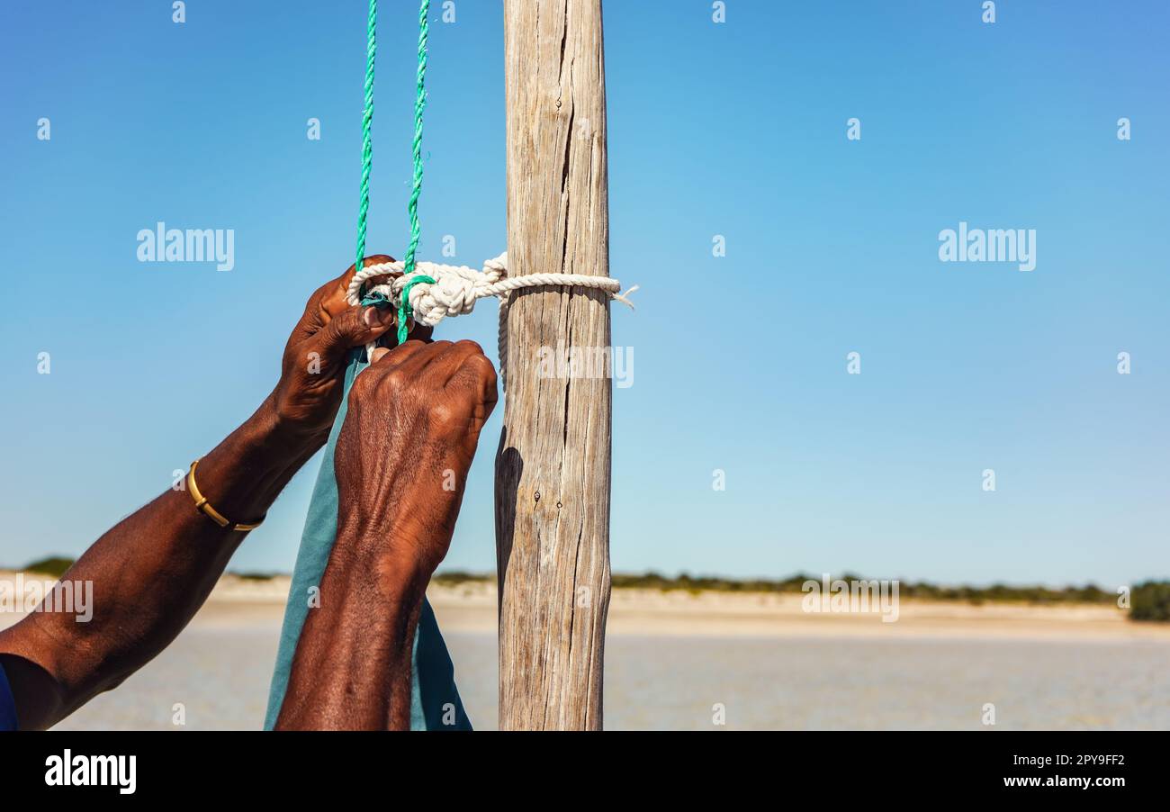 Ein lokaler madagassischer Mann, der ein Segelseil an einem Holzmast seines Schiffes befestigt, nur in den Händen Stockfoto