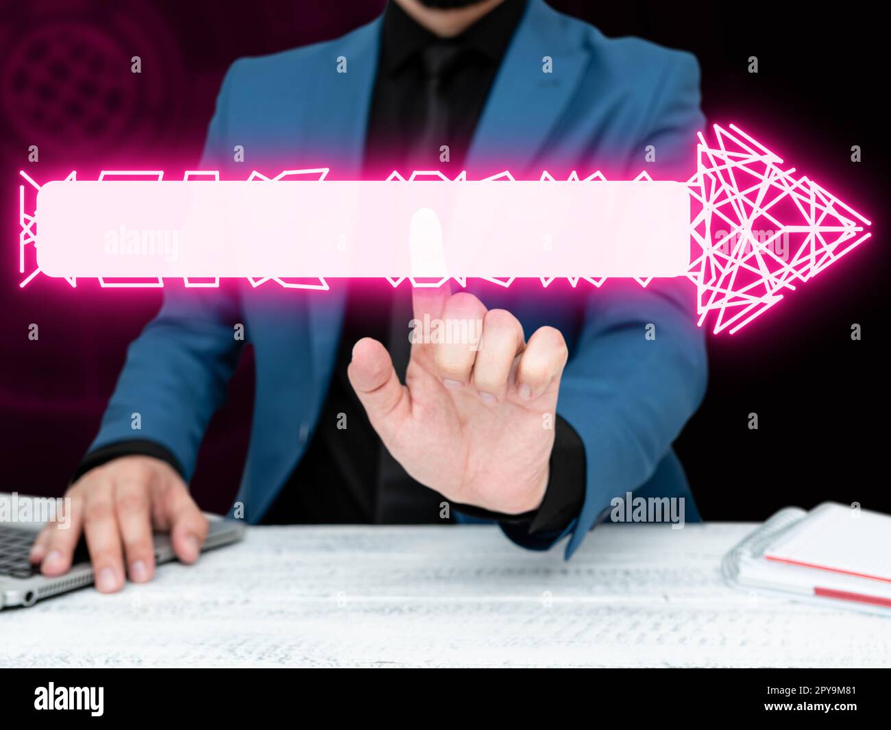Geschäftsmann in blauer Jacke sitzt am weißen Tisch und drückt virtuellen Knopf. Laptop liegt auf dem Schreibtisch. Futuristisches Bild mit farbigem Leuchten. Stockfoto