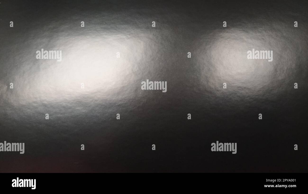 Lichtreflexionen auf glänzendem grauem Papier. Mehrere helle Flecken auf einer dunklen Oberfläche, die Licht reflektieren. Abstrakter einfarbiger Hintergrund. Stockfoto