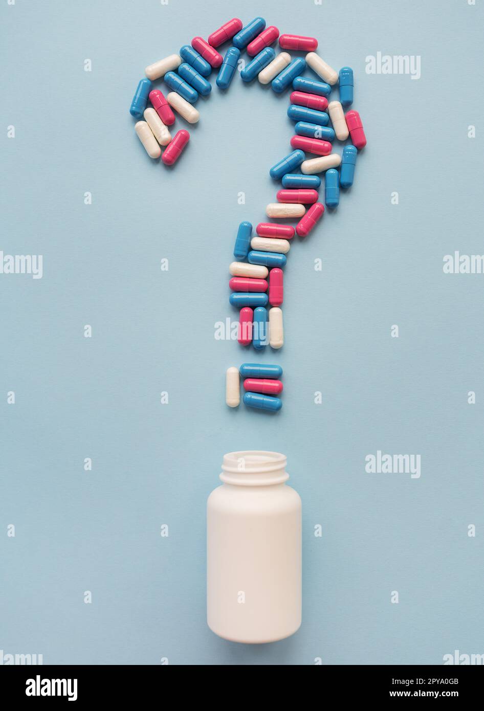 Ein Fragezeichen bestehend aus drei mehrfarbigen Vitaminen auf blauem Hintergrund und einer weißen Kunststoffflasche. Gesundheitsprobleme und Behandlung. Das Konzept der evidenzbasierten Medizin. Stockfoto