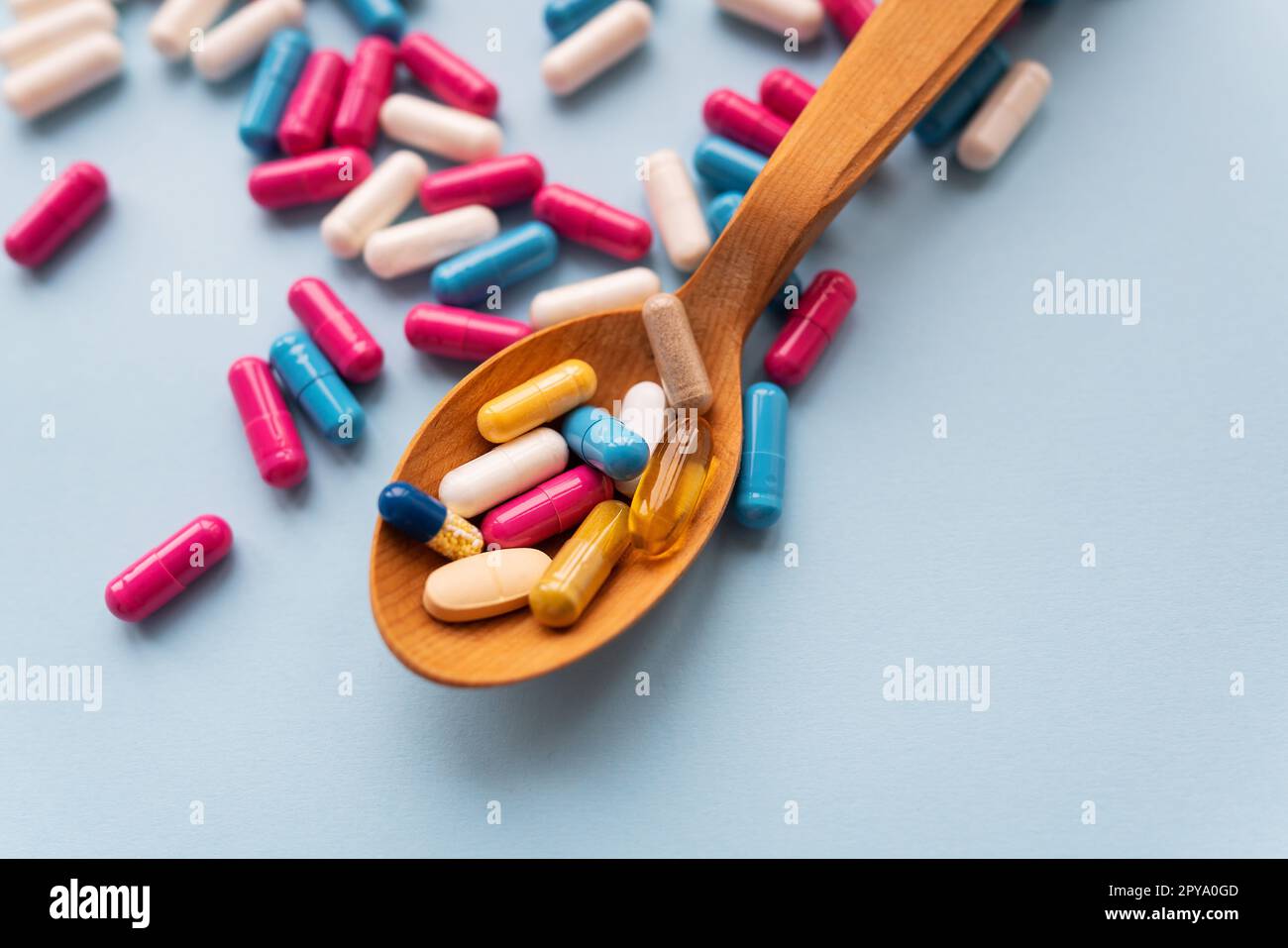 Verschiedene helle Pillen auf blauem Hintergrund liegen in einem Holzlöffel vor dem Hintergrund verschiedener heller Pillen. Gesundheitskonzept, Nahaufnahme. Stockfoto